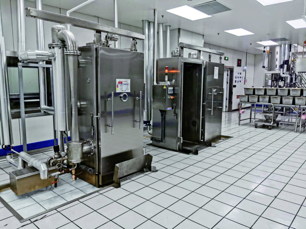 Stainless steel vacuum cooling machines in a clean food processing facility, equipped with industrial piping and control panels.