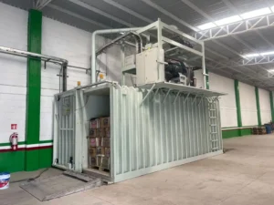 Installed Allcold vacuum cooler with machinery above the chamber and stacked cartons visible through the open doorway