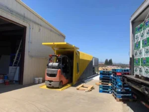 Real yellow Allcold vacuum cooler beside a warehouse, forklift, pallets and a loaded produce truck