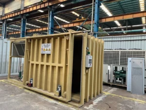 Allcold yellow vacuum chamber with a sliding door and adjacent refrigeration equipment on the factory floor