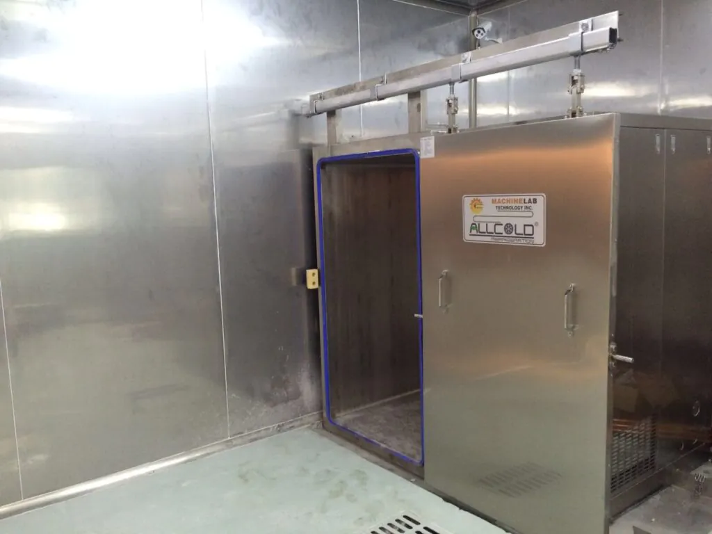 A stainless steel vacuum cooling machine installed in a commercial kitchen, with its door open showing the inner chamber for rapid cooling of cooked food.