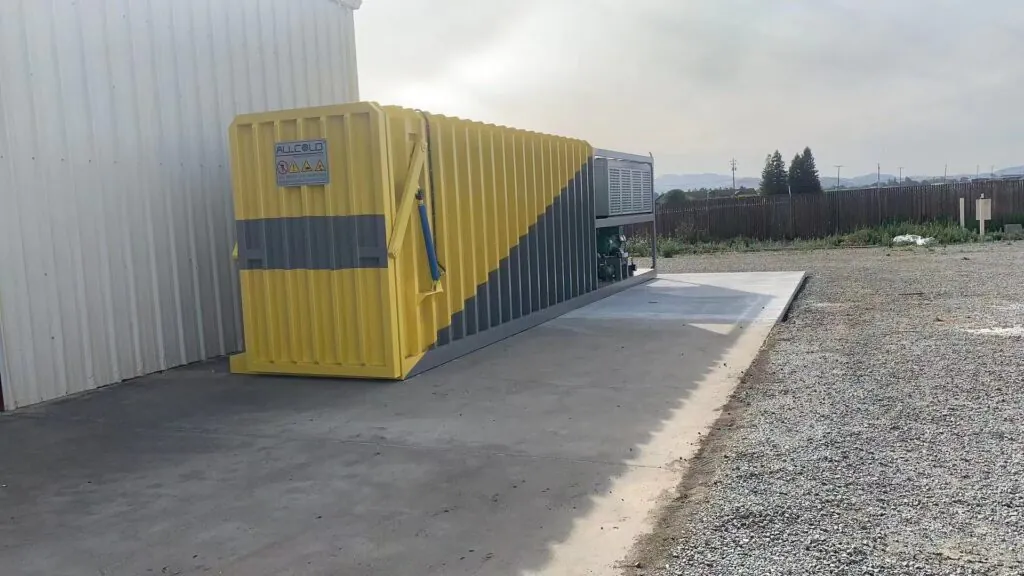 Allcold outdoor vacuum cooling machine for fresh produce with custom yellow and gray coating installed beside a vegetable processing warehouse