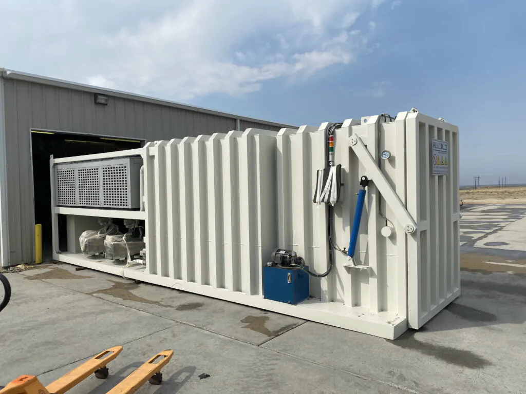 Outdoor installation of a commercial vacuum cooling machine near a warehouse, showing the condenser unit and hydraulic control system on a reinforced concrete base.
