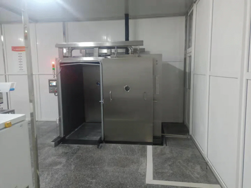 Commercial vacuum cooling chamber with open door, installed in a clean food processing facility for rapid cooling of cooked products.