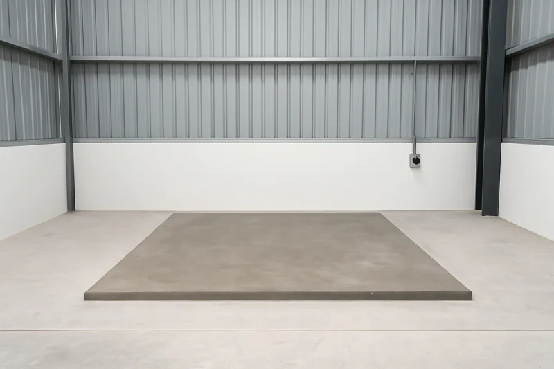 A clean, well-lit area in a warehouse with a new concrete pad and a dedicated industrial power outlet on the wall, ready for installation.