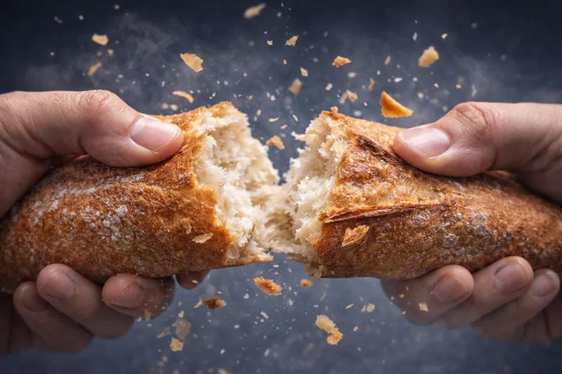 A close-up shot of a hand breaking a vacuum-cooled baguette, with crispy shards flying off, demonstrating the perfect texture.