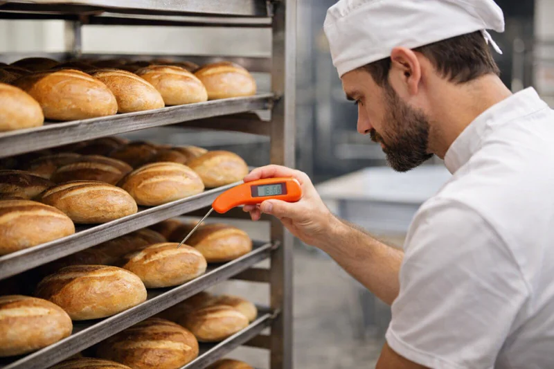 baker checking temperature of bread loaves on a rack