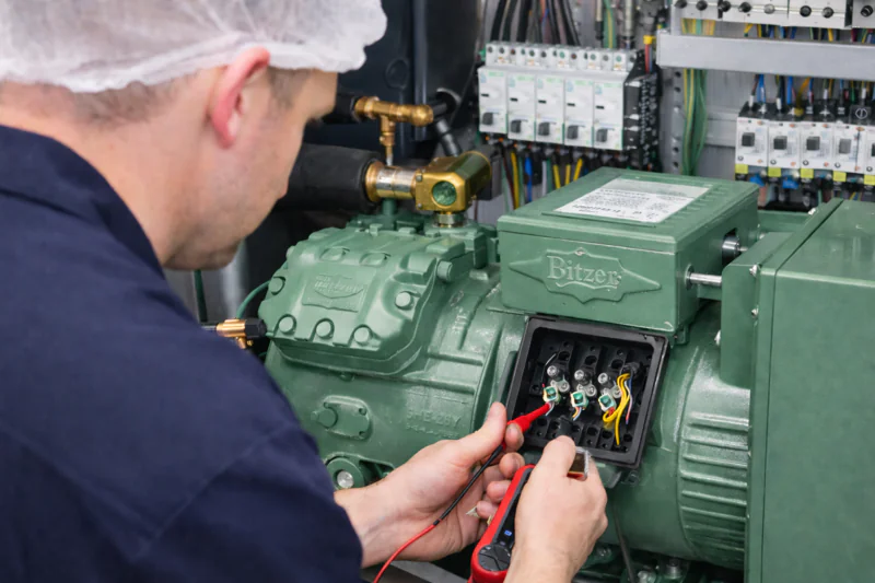A technician inspecting the internal components of a vacuum cooler, specifically focusing on the Bitzer compressor