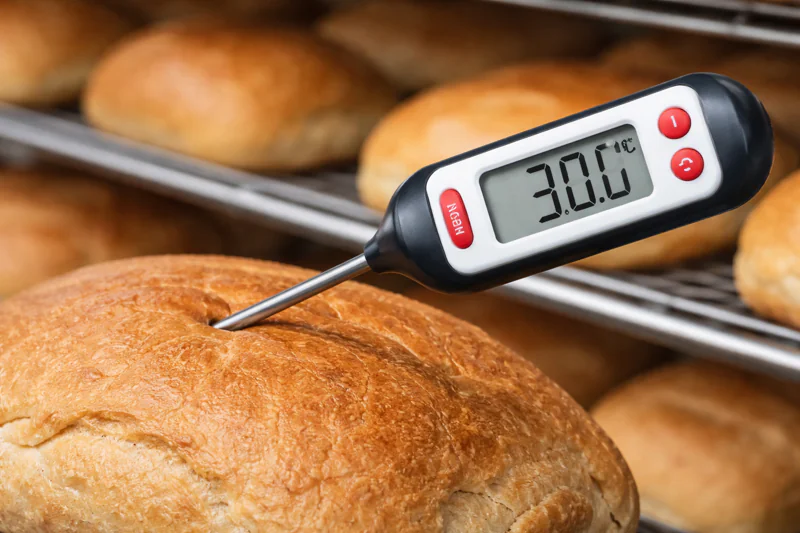 A close-up of a digital thermometer probe inserted into a loaf of bread showing 30°C