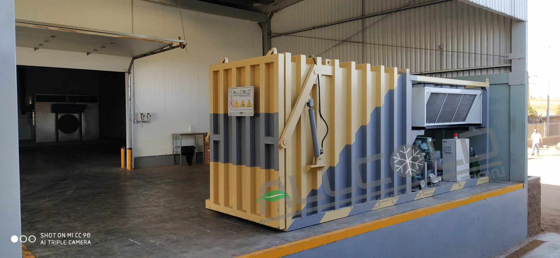 Real yellow and grey Allcold vegetable vacuum cooler installation showing the hydraulic outward-opening door linkage
